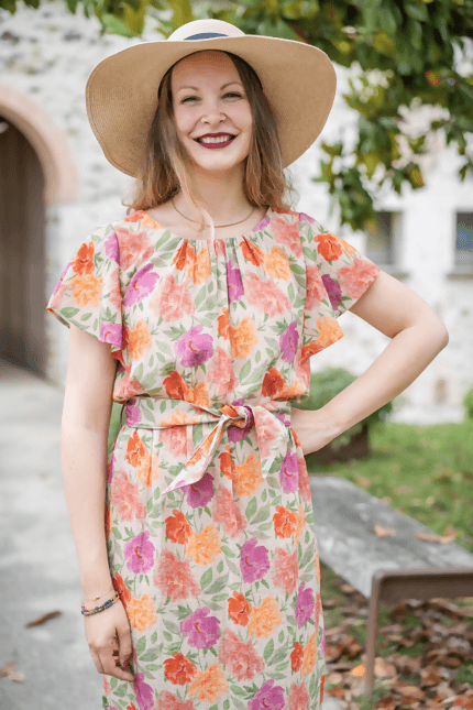 Femme souriante portant une robe FLORISSE colorée avec manches volantées et chapeau, idéale pour le printemps.