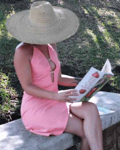 Femme portant une Robe Hécate - T36 à 50, décolleté plongeant, lisant dehors sous un chapeau, patron de couture pdf à télécharger.