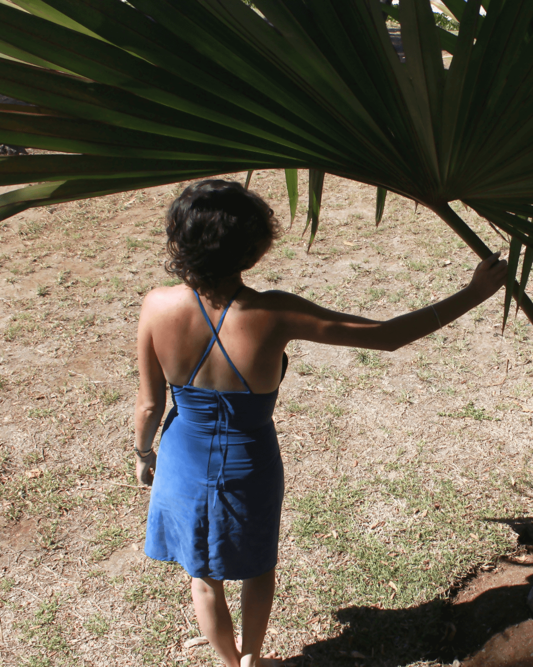 Femme en robe dos nu bleue sous un palmier, mettant en valeur le modèle Robe Hécate - T36 à 50, patron de couture pdf à télécharger.