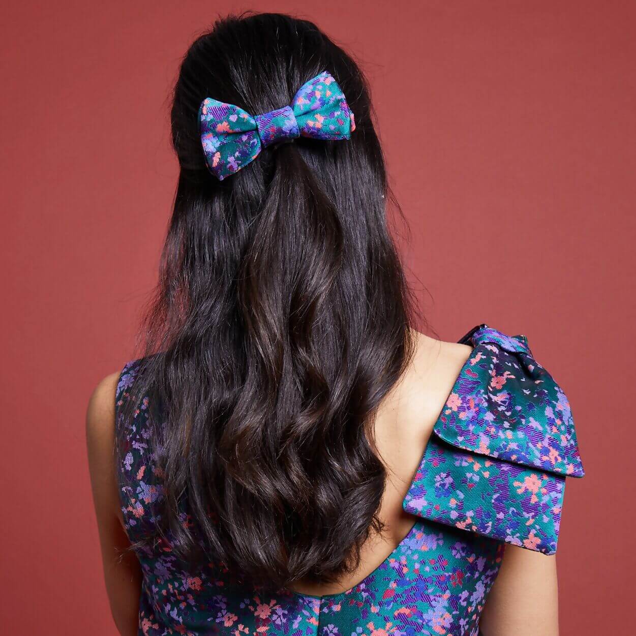 Femme portant une robe floral avec un nœud dans les cheveux, représentant le style de la Robe L'Audacieuse - T34 à 48.