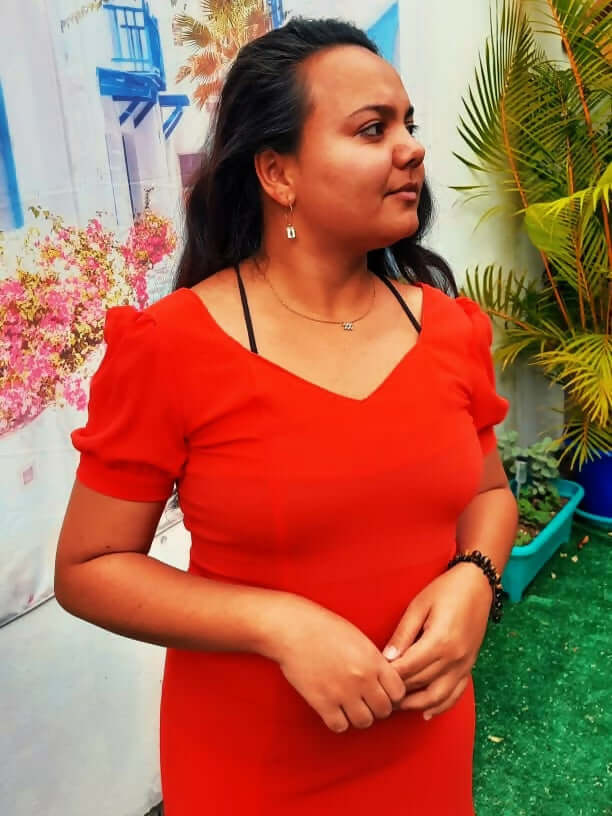 Femme portant une robe rouge à manches ballons, arrière-plan coloré avec des plantes et fleurs.