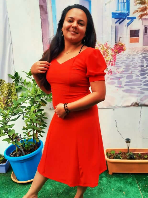Femme portant une robe rouge avec des manches ballons, dans un décor floral et verdoyant.