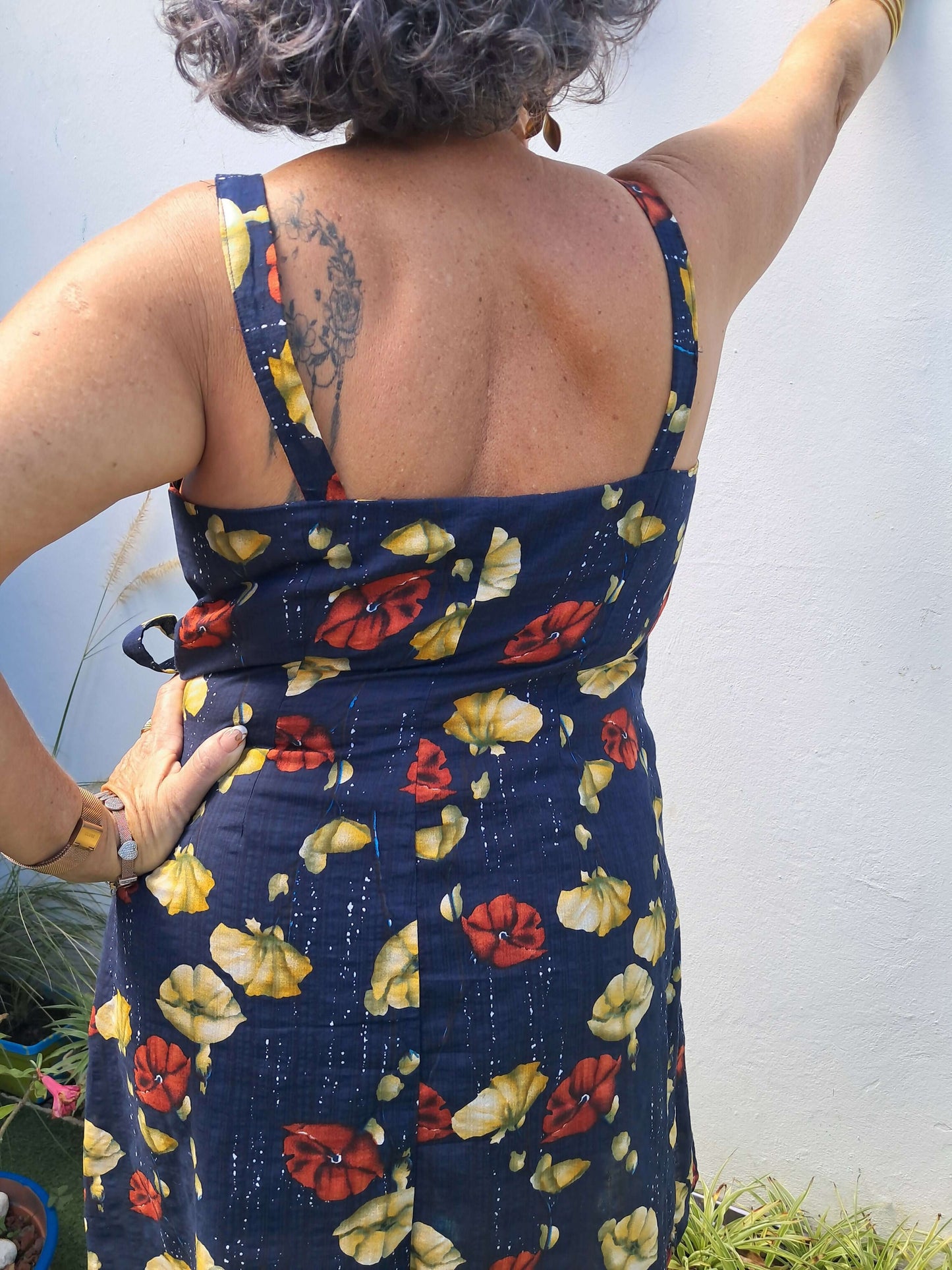 Femme portant une robe portefeuille à bretelles, vue de dos, avec un motif floral coloré et un ourlet arrondi.