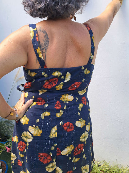 Femme portant une robe portefeuille à bretelles, vue de dos, avec un motif floral coloré et un ourlet arrondi.