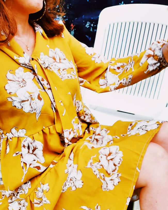 Femme portant une robe jaune à fleurs, assise sur une chaise, mettant en avant le style et le confort.
