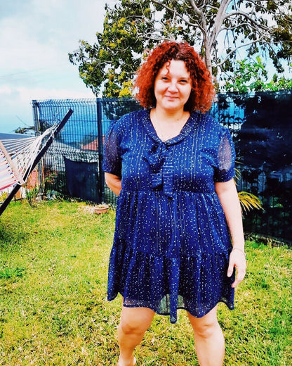 Femme portant une robe babydoll Sothis en bleu marine, style vintage, au milieu d'un jardin.