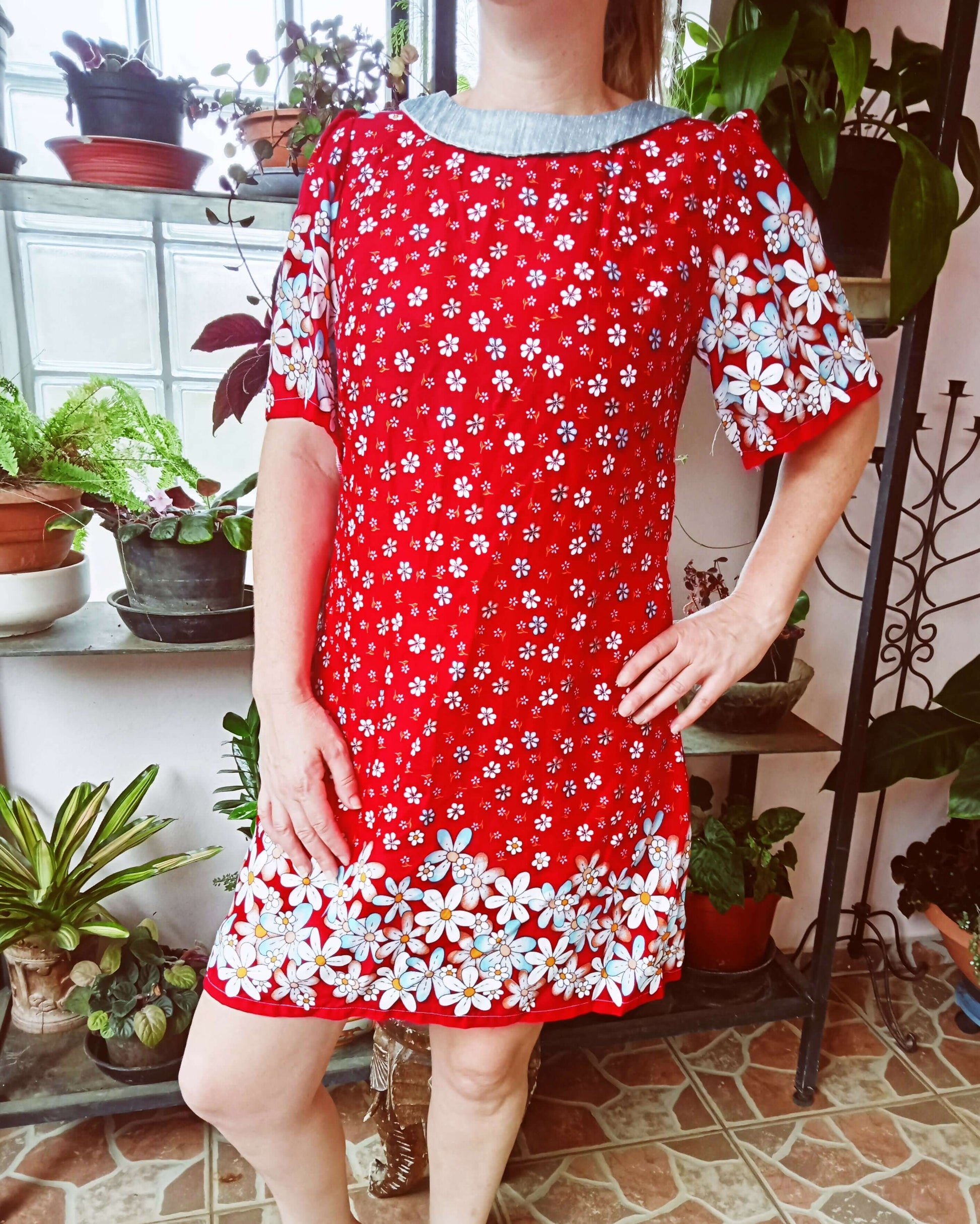 Robe rouge à fleurs avec manches évasées, présentée dans un environnement de plantes d'intérieur.