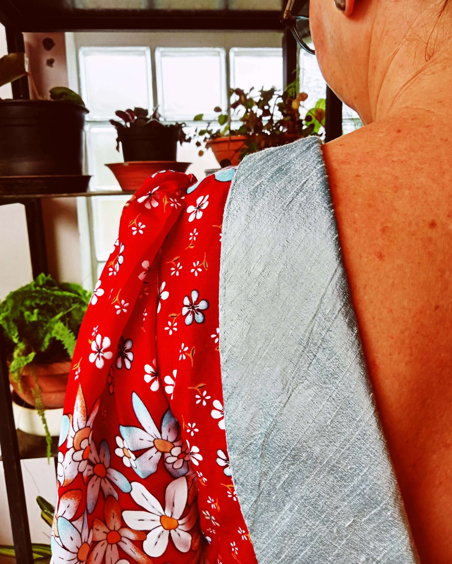 Détail d'une robe avec manches froncées et décolleté dans le dos, dans un décor de plantes d'intérieur.