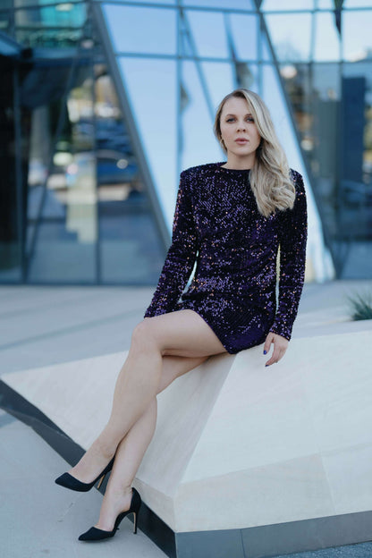 Robe - XS-XL - ARTISTA modèle en sequins violets, photo de femme assise dans une ambiance moderne.