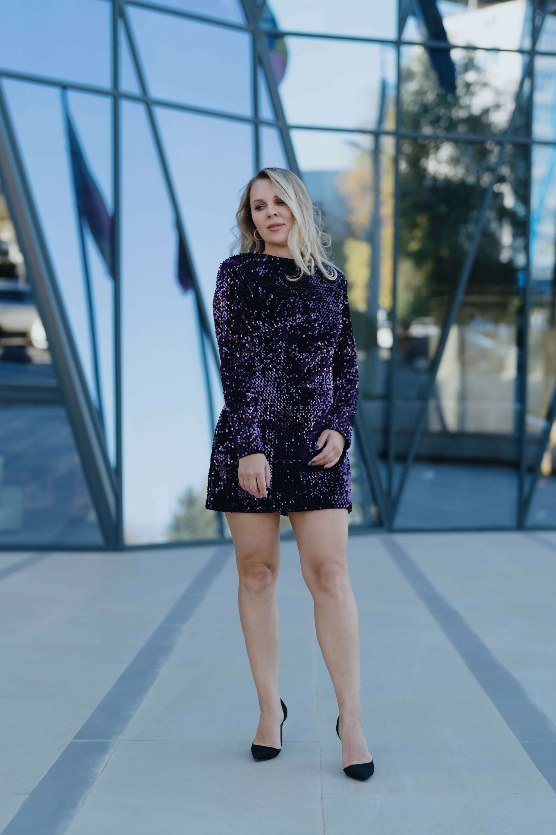 Robe - XS-XL - ARTISTA en velours violet, design moderne, modèle femme posant devant des reflets de verre.