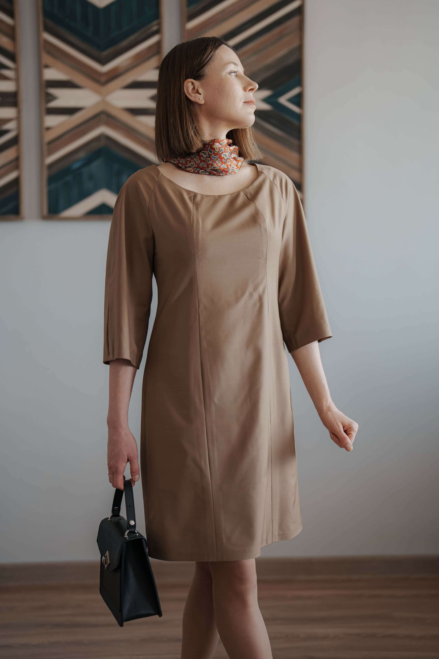 Femme portant la robe beige "Robe - XS/XL - SOFIA" avec sac noir, modèle de patron de couture pdf à télécharger.