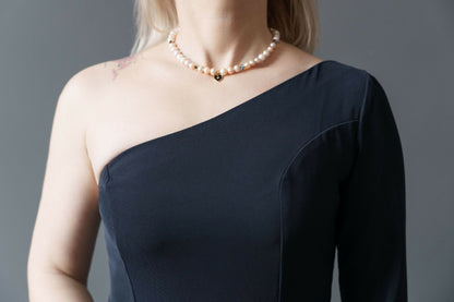 Femme portant une robe noire à une manche avec un collier de perles