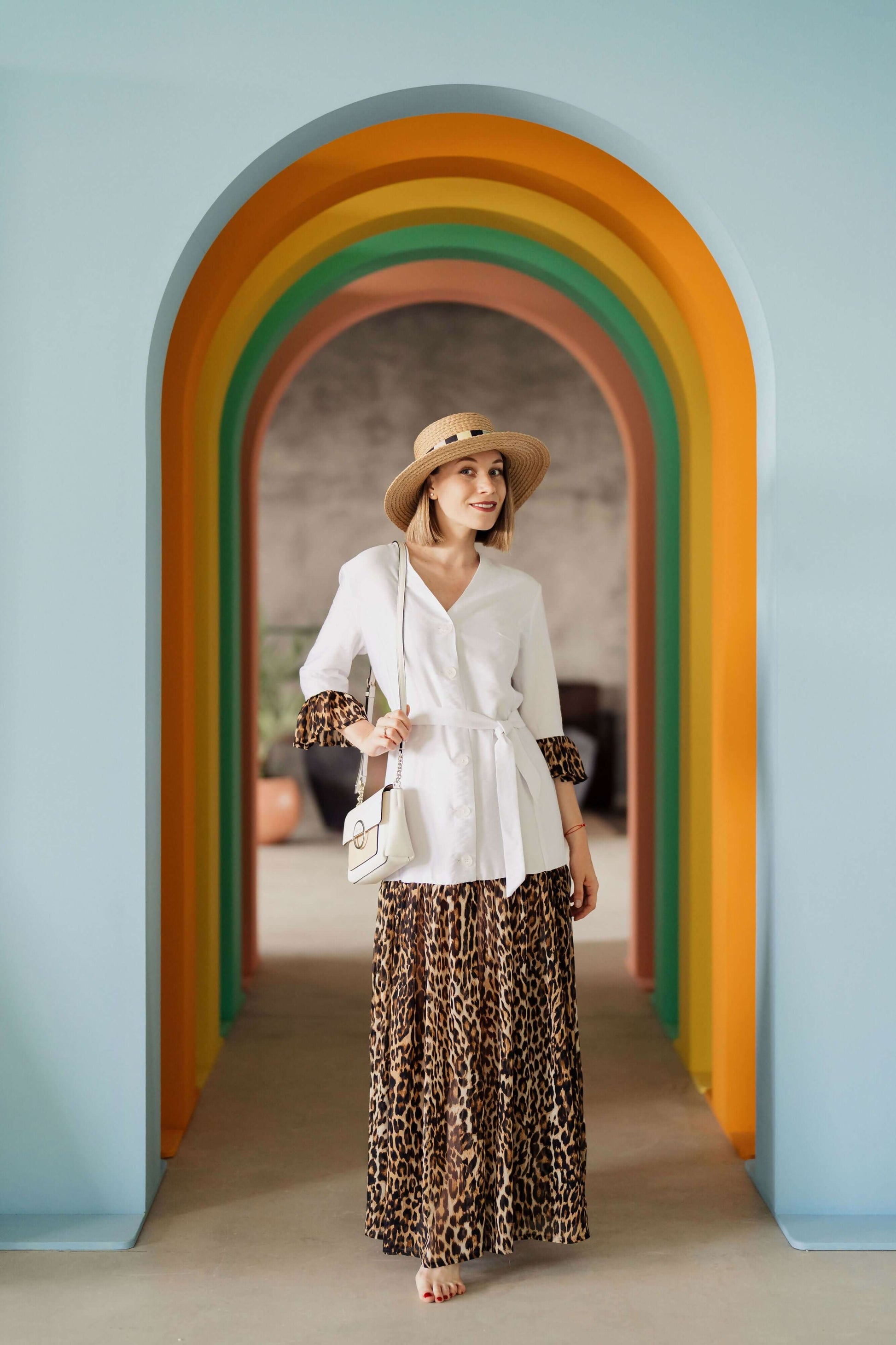 Femme en tenue décontractée sous un arc-en-ciel de couleurs, portant un chapeau et une robe imprimée léopard.