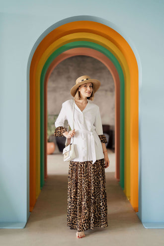 Femme en tenue décontractée sous un arc-en-ciel de couleurs, portant un chapeau et une robe imprimée léopard.