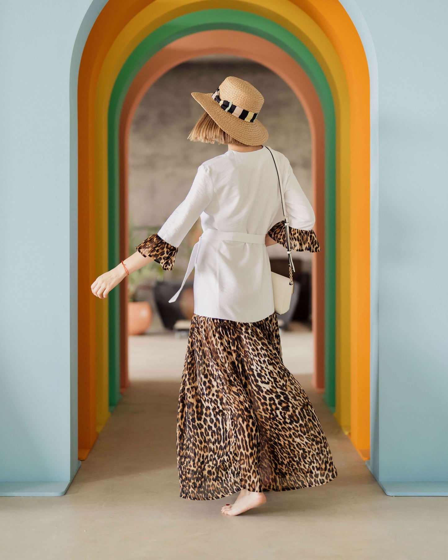 Femme portant une robe motif léopard, debout dans un couloir coloré.