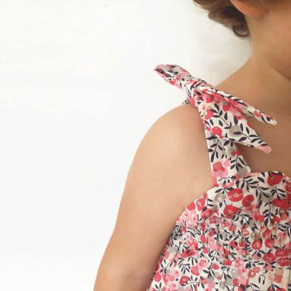 Enfant portant une robe à smock (facile) Porquerolles, patron de couture PDF à télécharger, bretelles nouées, tissu fleuri.