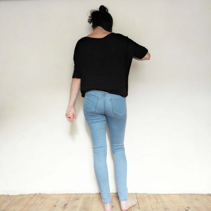 Femme vue de dos portant un top noir et un jean bleu clair sur un fond neutre, mettant en valeur le style décontracté.