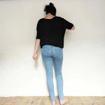 Femme vue de dos portant un top noir et un jean bleu clair sur un fond neutre, mettant en valeur le style décontracté.