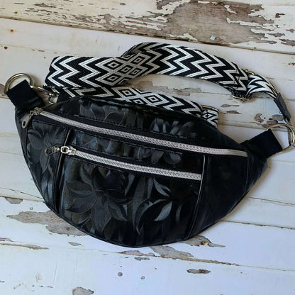 Sac banane Amaya noir à motifs floraux, avec bandoulière ajustable et poches zippées, style chic et pratique.