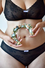 Femme avec lingerie noire en dentelle tenant un accessoire floral autour de la taille, parfait pour un look élégant.