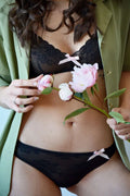 Femme en lingerie noire avec des détails en dentelle, portant une veste verte et tenant des fleurs roses.