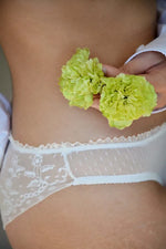 Une femme portant des dessous en dentelle avec des fleurs vertes en main, représentant l'élégance et le confort.