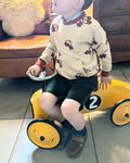 Enfant portant le Sweat AVENTURIER - Patron de couture PDF Enfant du 2 au 16 ans, assis sur une voiture jouet jaune, patron de couture pdf à télécharger.