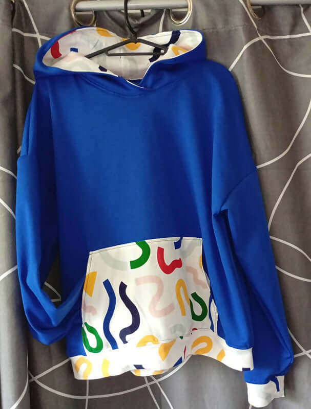 Sweat S pour Lui avec capuche, patron de couture PDF à télécharger, couleur bleu vif avec motifs colorés, idéal pour un style décontracté.