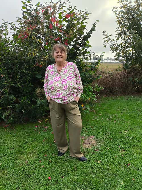 Personne portant une chemise fleurie dans un jardin, visiblement joyeuse, avec une végétation luxuriante en arrière-plan.