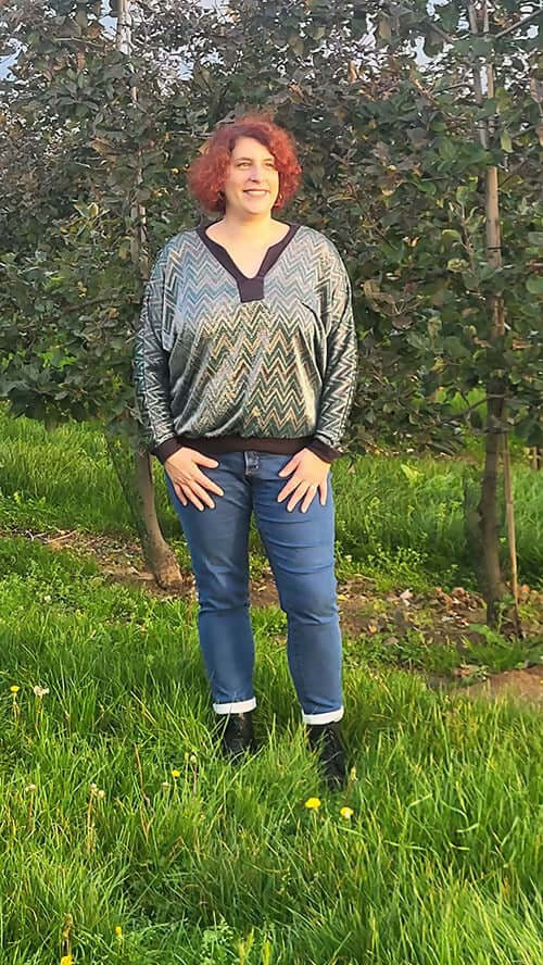 Femme portant un chandail à motifs dans un verger verdoyant.