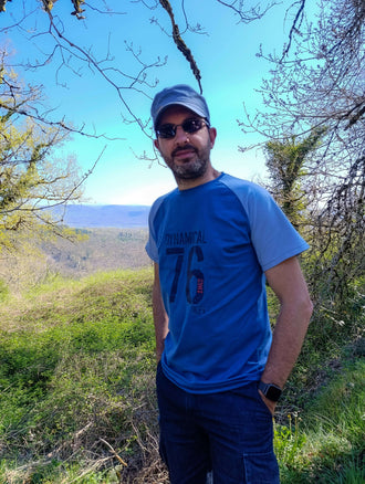 Homme en tee-shirt bleu, lunettes de soleil, en pleine nature avec vue sur la vallée.