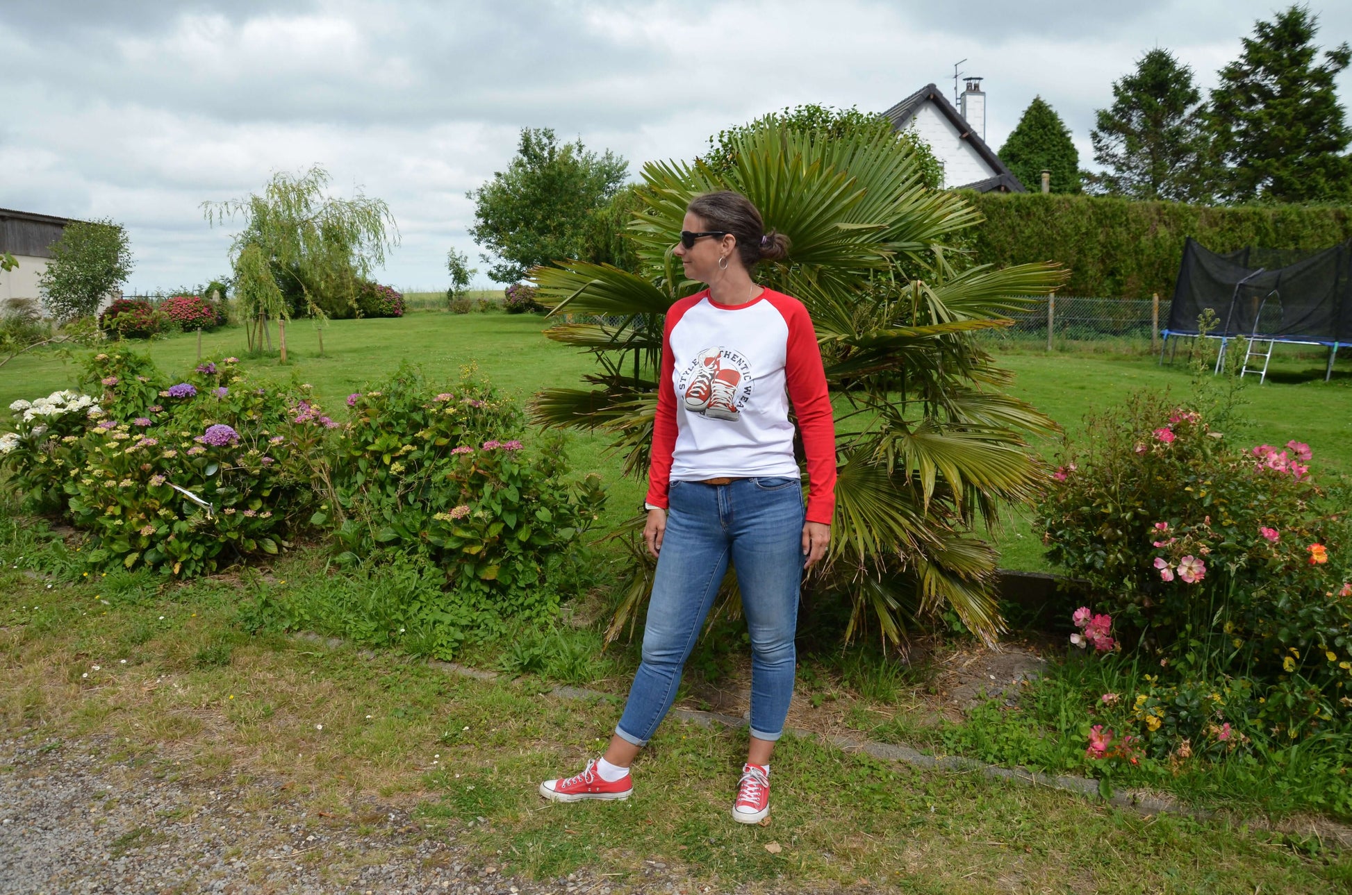 Femme portant un T-shirt à manches raglan rouge, dans un jardin verdoyant, style décontracté.