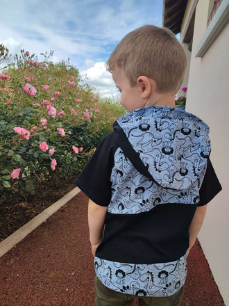 Garçon portant un T-shirt Loulou avec capuche, motif amusant, face à des fleurs roses.