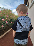 Garçon portant un T-shirt Loulou avec capuche, motif amusant, face à des fleurs roses.