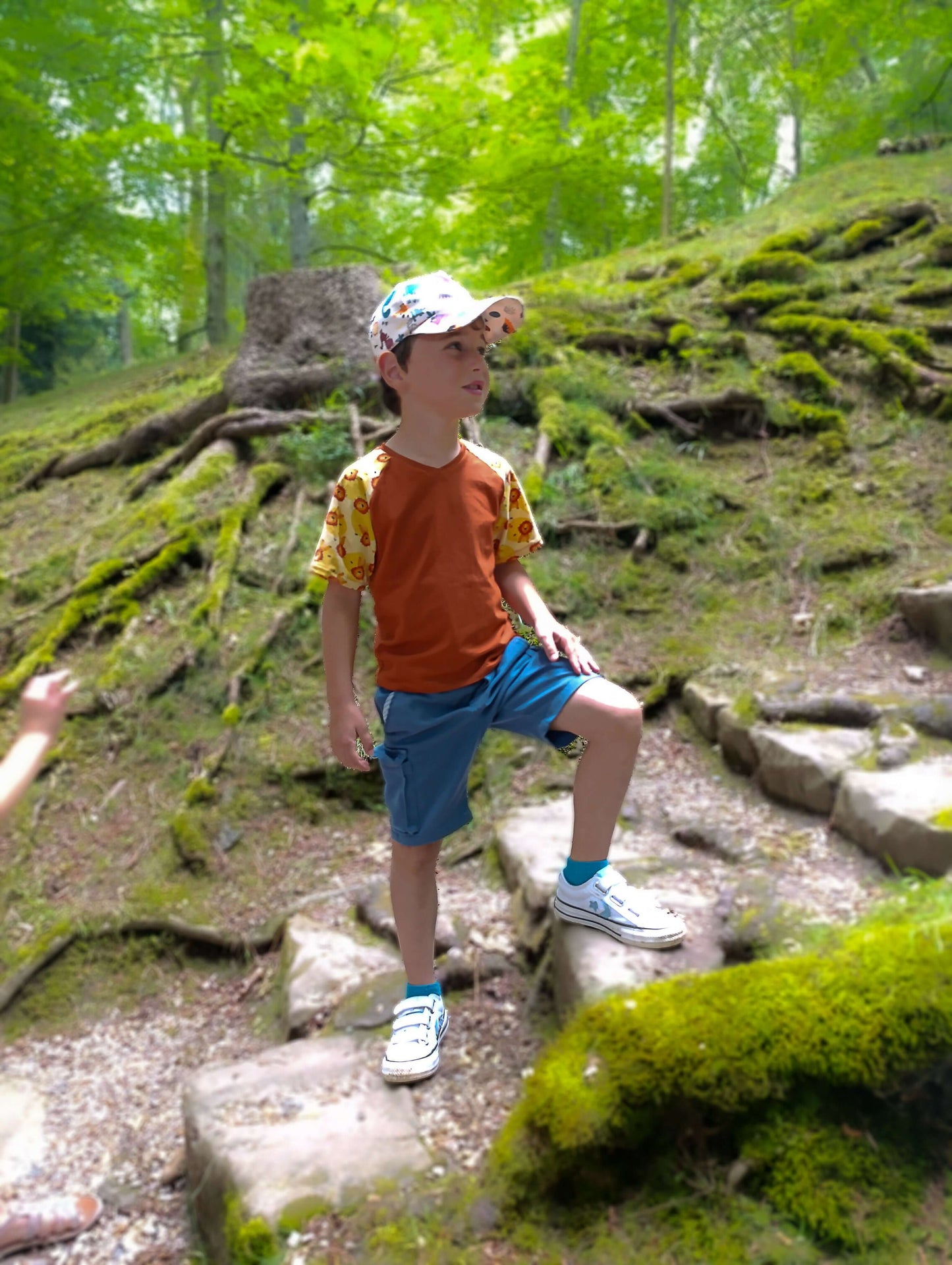 Enfant portant un T-shirt Loulou orange dans une forêt, explorant les marches en pierre.