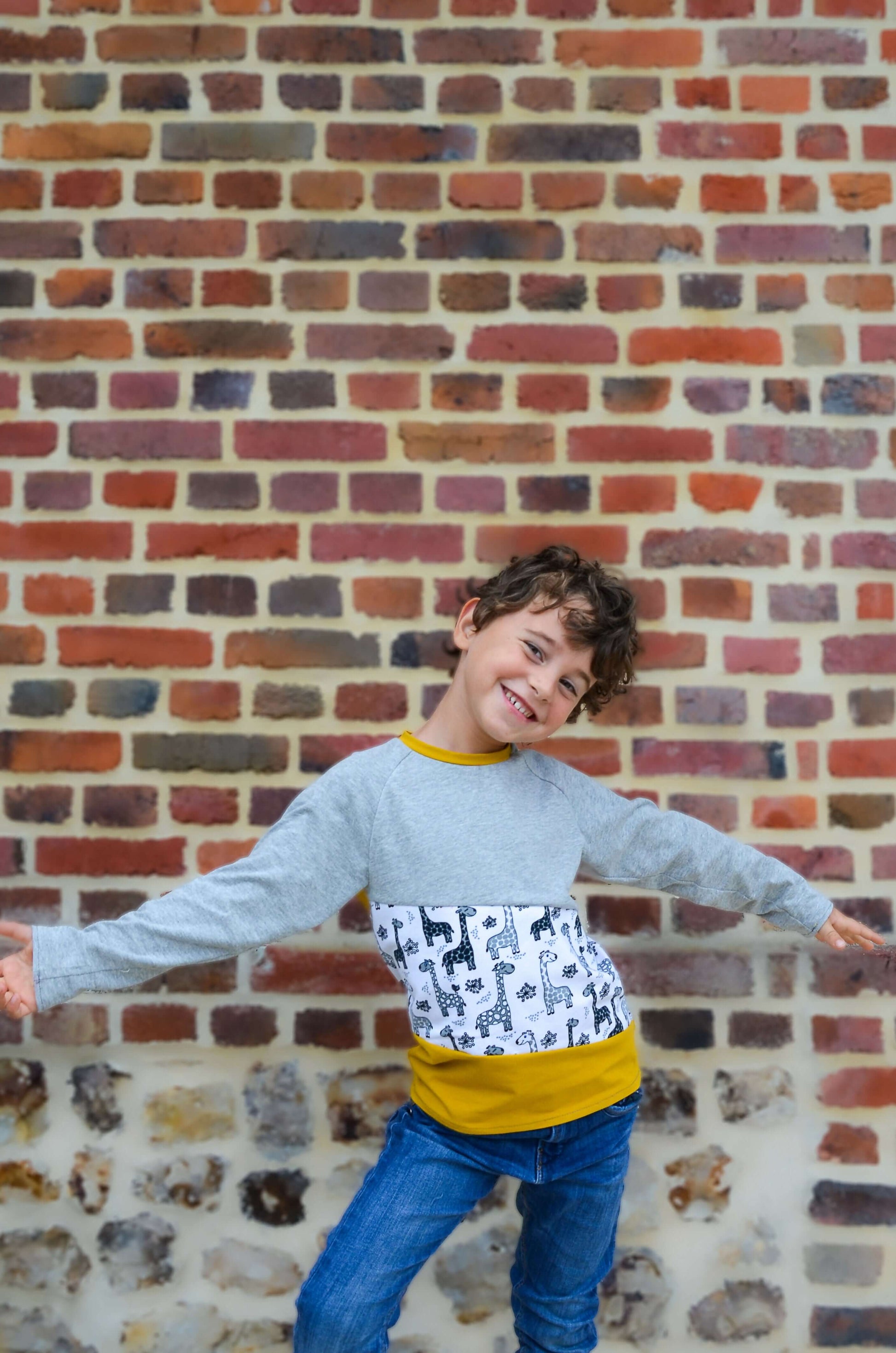 Enfant heureux portant un t-shirt coloré devant un mur en briques, style moderne et amusant.