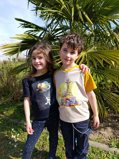 Deux enfants souriants portant des T-shirts colorés avec des motifs, derrière une plante d'extérieur.