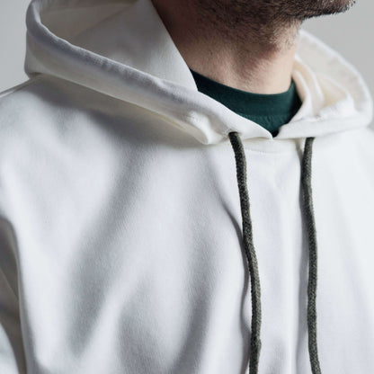 Gros plan d'un sweat à capuche blanc porté par un homme, cordons de couleur sombre visibles.