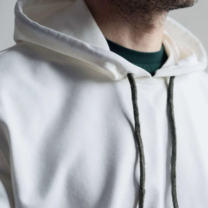 Gros plan d'un sweat à capuche blanc porté par un homme, cordons de couleur sombre visibles.