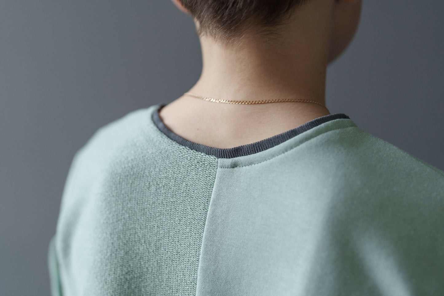 Vue arrière d'un T-shirt vert menthe avec un détail de couture sur la nuque, porté par un modèle avec un collier subtil.