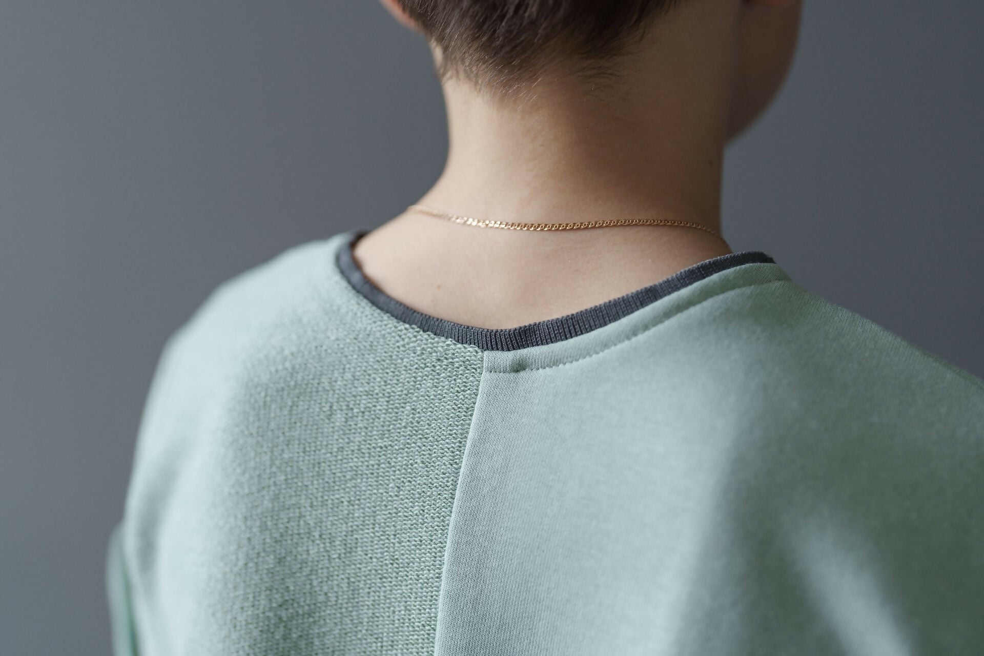 Vue arrière d'un T-shirt vert menthe avec un détail de couture sur la nuque, porté par un modèle avec un collier subtil.