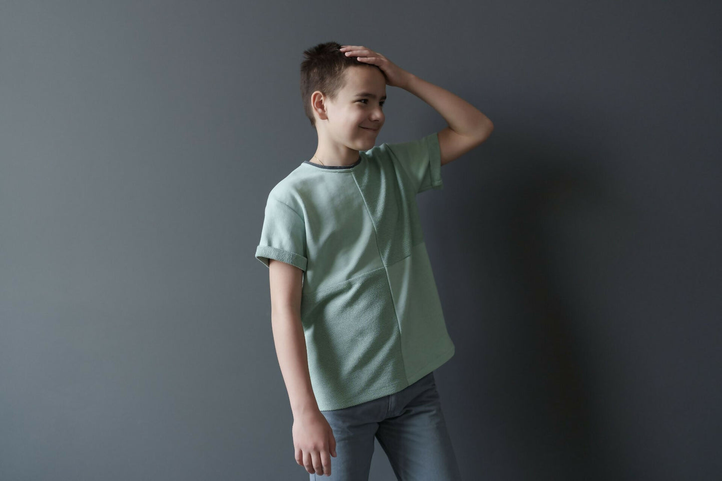 Garçon portant un t-shirt vert pastel en coton, souriant devant un fond gris.
