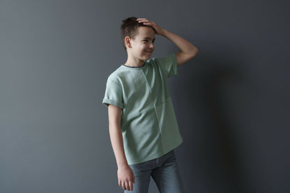 Garçon portant un t-shirt vert pastel en coton, souriant devant un fond gris.