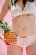 Femme portant lingerie en dentelle blanche, tenant un ananas, arrière-plan rose. Style sexy et féminin.