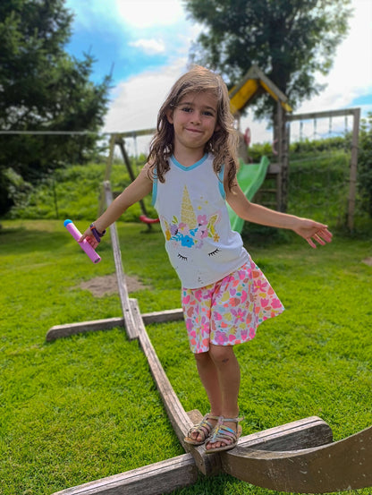 Fille jouant à l'extérieur avec un haut décoré d'une licorne et une jupe colorée, s'amusant sur un terrain de jeu.