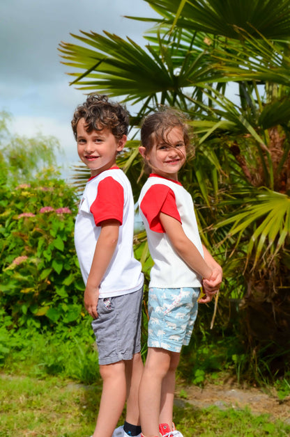 Deux enfants souriants portant des t-shirts à manches courtes rouges dans un jardin verdoyant.