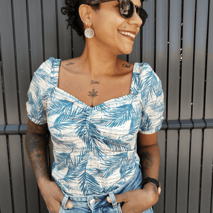 Femme souriante portant un top Touraco à motifs de feuilles, décolleté carré et manches bouffantes.