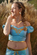 Femme portant un haut bleu avec détails dorés, fond nature. Top Yasmine Femme - Patron couture du 32 au 56. Patron de couture PDF à télécharger.