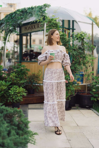 Femme portant un ensemble top et jupe longue style bohème - XS/XL - EL PASION avec un gobelet de café, fond de jardin urbain.