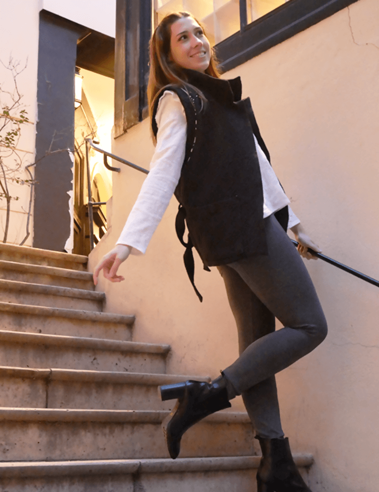 Femme souriante portant une veste Bogota élégante sur des escaliers, alliant confort et style.